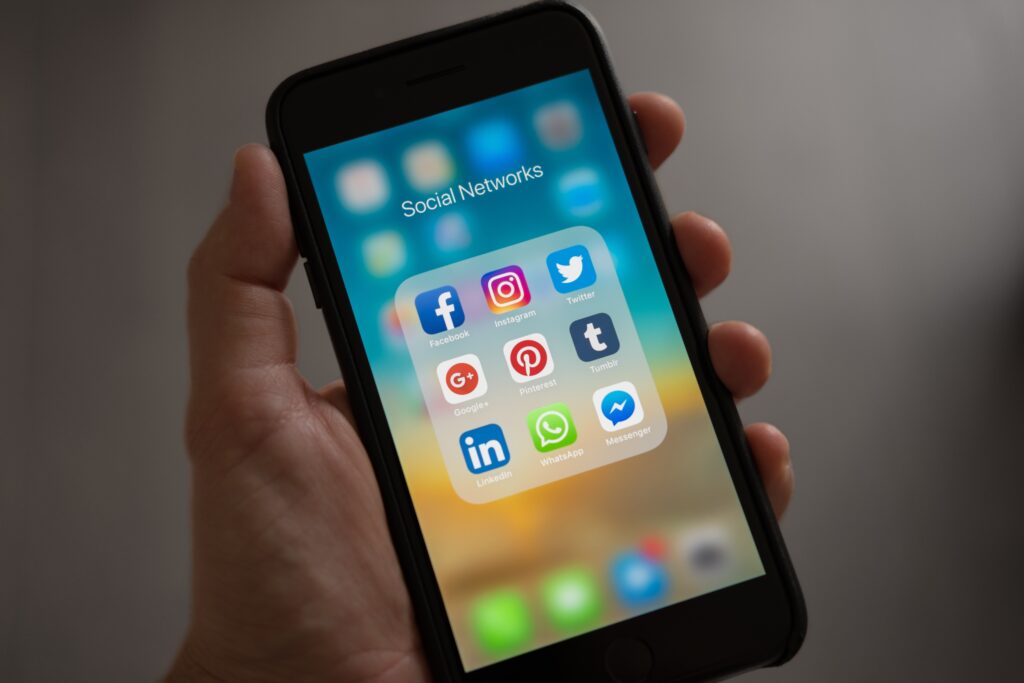 a hand holds a mobile phone, on the screen is social media network app icons