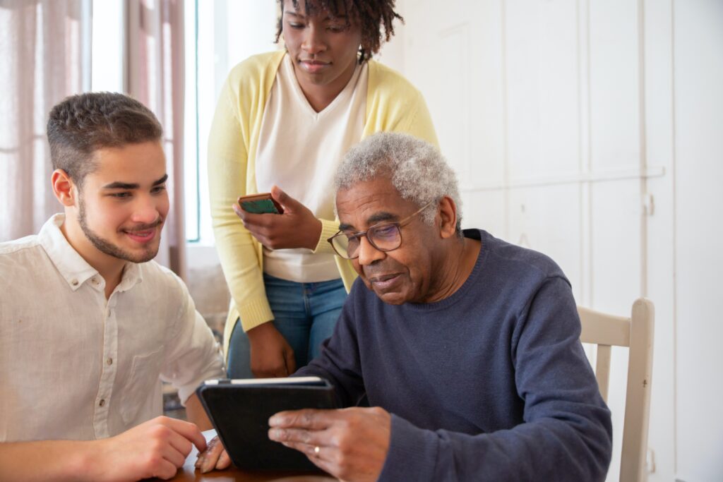two carers with and older man, the older man is holding a tablet device