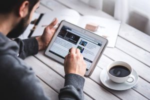 man using tablet with cup of coffee at table