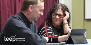 man and lady sitting at a table, talking and smiling with a tablet