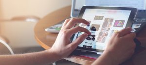 hands holding tablet with computer in background