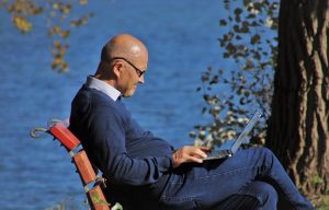 elderly man sitting outside on a bench with a laptop