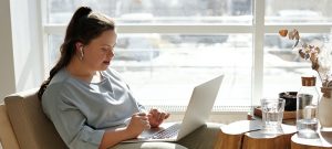 woman sitting on armchair with laptop and airpods