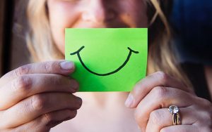 a woman's hands holding a green post-it with a black smile drawn on it with marker