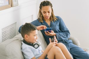 a child and a woman sit on a couch with their mobile phones in hand