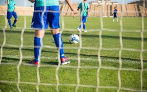 a wide shot of a soccer field with kids legs, grass, a ball and a soccer net