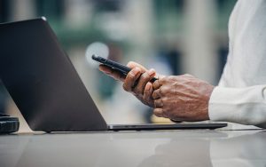 a laptop on a table, a person's hands holding a mobile phone