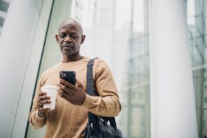 an elderly man stands holding a mobile phone and a cup of coffee